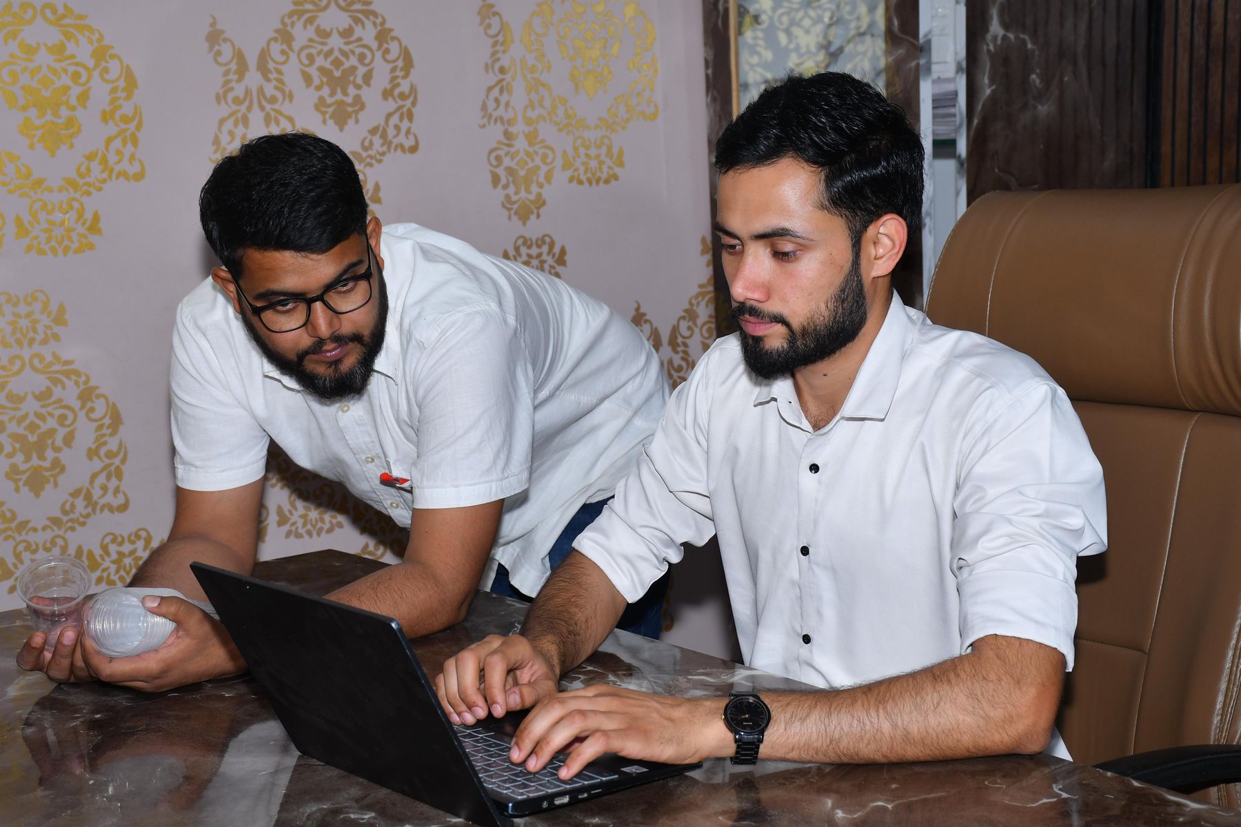 Two Pakistani developers working through code together on a laptop