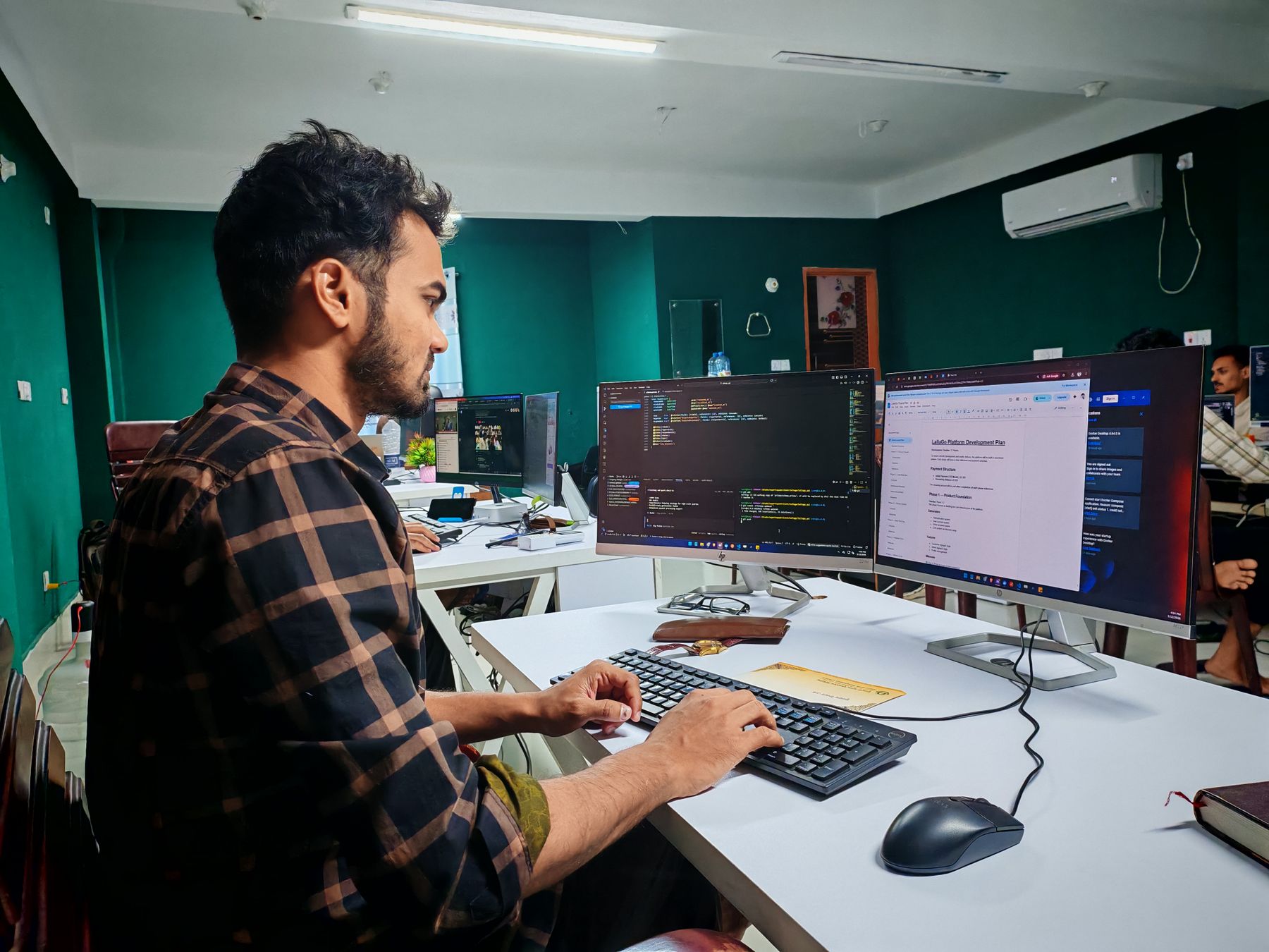 A Pakistani developer coding at a two-screen desk